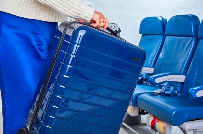 Individual carrying a hardside suitcase near airplane seating