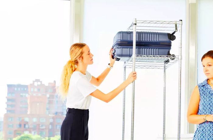 Individual placing the carry-on from the Béis Hardside Luggage Set on a high shelf while another person stands close by