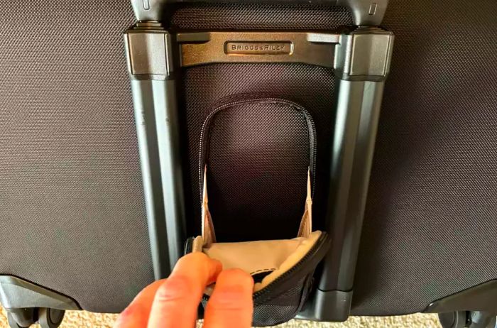 A hand unzipping a pocket on the exterior of the Briggs & Riley Baseline 21-inch Carry-on Wheeled Garment Spinner