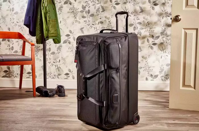 The Tumi Large Split 2-Wheeled Duffel displayed against a backdrop of floral wallpaper and a coat rack