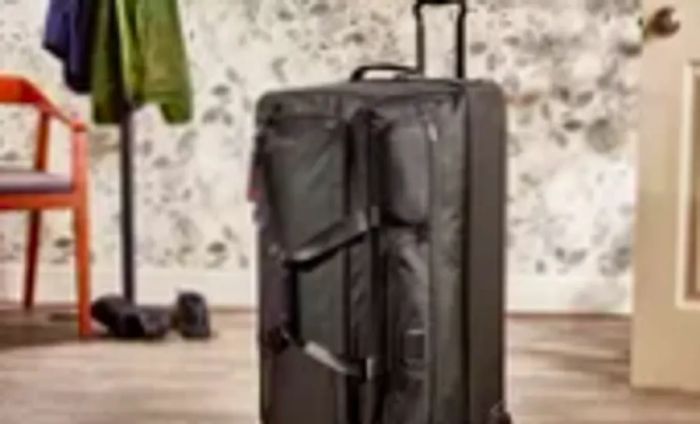 The Tumi Large Split 2-Wheeled Duffel positioned in front of floral wallpaper and a coat rack