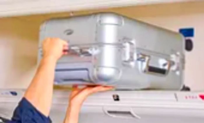 A person places the Zero Halliburton Classic Aluminum 3.0 International Carry-on into an overhead bin