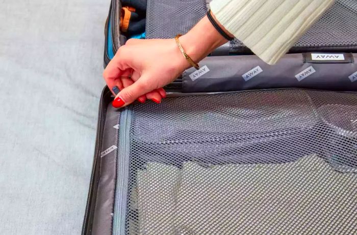 A hand zipping up an inner pocket of the Away Luggage Set