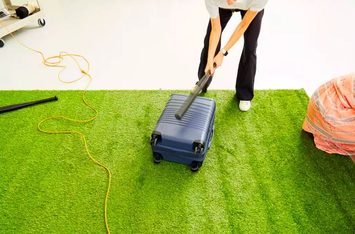 Individual striking the Béis Hardside Luggage Set with a baseball bat on synthetic turf