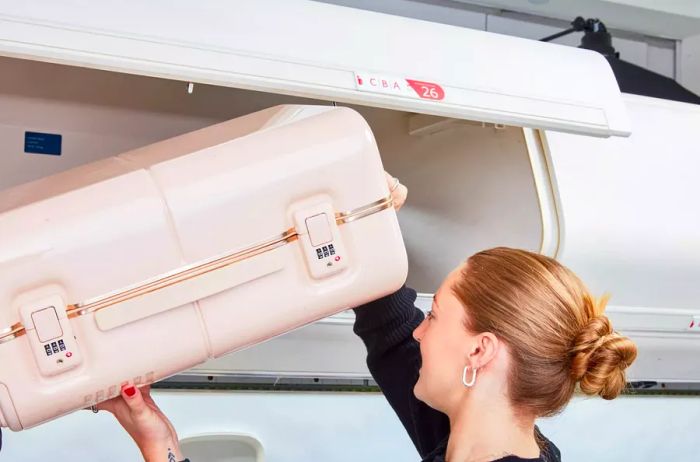 A traveler placing the July Carry On Trunk into the airplane's overhead compartment