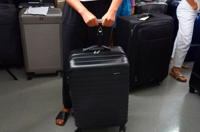 Hands using a luggage scale to weigh the Amazon Basics 20-inch Hardside Spinner