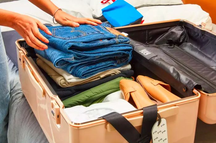 Hands organizing clothes inside the July Trunk Set suitcase