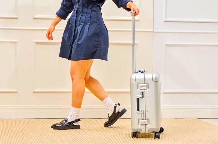 A person rolls the Zero Halliburton Classic Aluminum 3.0 International Carry-on 33L over a carpeted surface