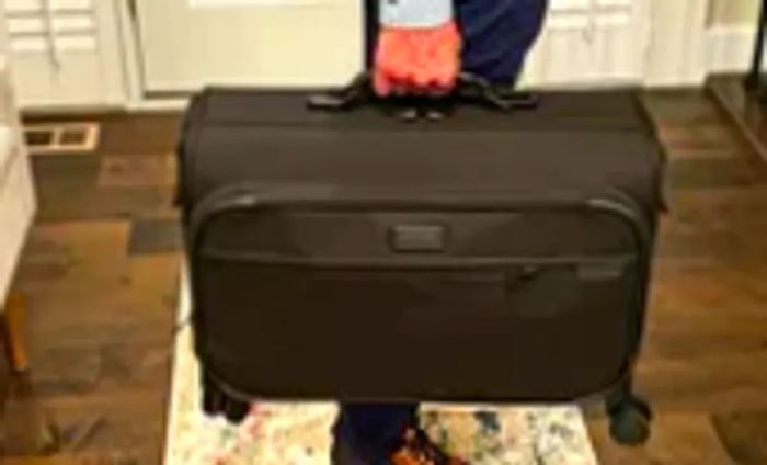 A person lifting the Briggs & Riley Baseline 21-inch Carry-on Wheeled Garment Spinner by its handle