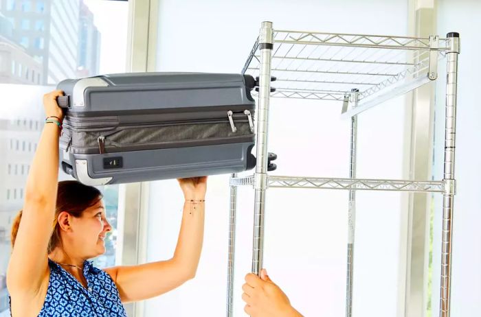 Individual placing the Travelpro Platinum Elite Carry-on/Large Check-in Hardside Luggage Set onto a high shelf