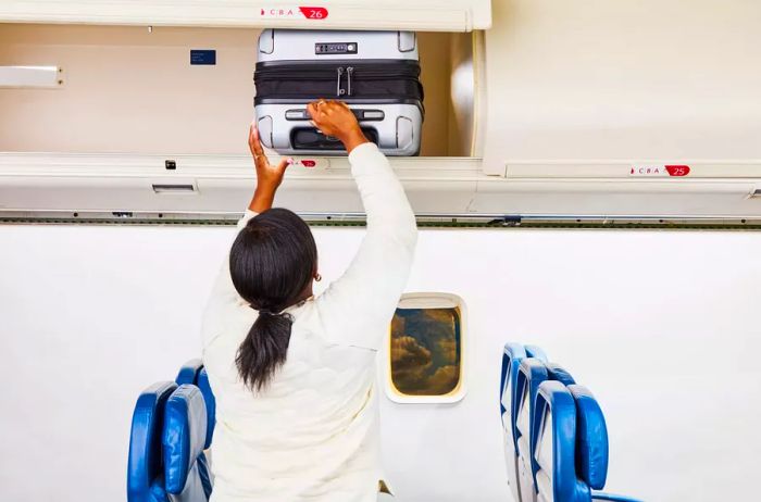 An individual placing the Travelpro Roundtrip Carry-On into an overhead compartment