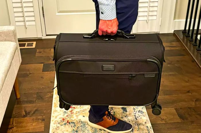 A person lifting the Briggs & Riley Baseline 21-inch Carry-on Wheeled Garment Spinner by its handle