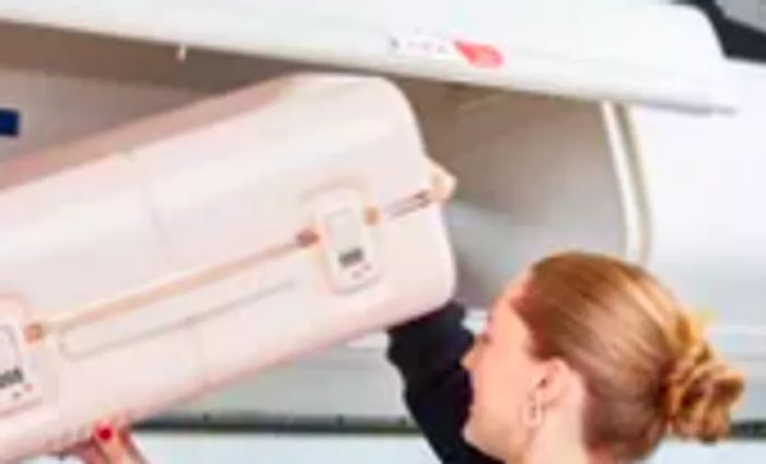 Individual placing the July Carry On Trunk in the airplane's overhead compartment