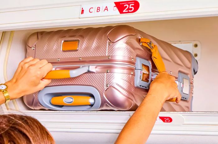 An individual placing the TUMI 19 Degree Aluminum International Carry-on into an overhead bin on an airplane