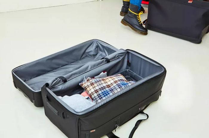 The Tumi Alpha 3 Large Split 2-Wheeled Duffel sits on the floor, partially filled with clothing