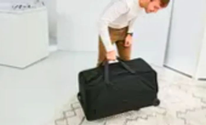 A person lifting the Tumi Alpha 3 Large Split 2-Wheeled Duffel off a white and gray rug