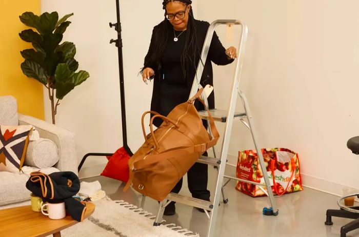 A person pushes a Leatherology Kessler Large Duffle off a step ladder