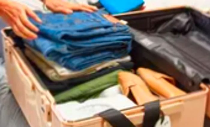 Hands packing clothes into the July Trunk Set case