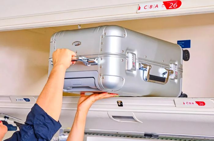 A person stowing the Zero Halliburton Classic Aluminum 3.0 International Carry-on in an overhead bin