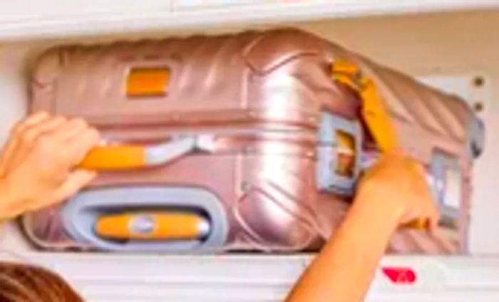 An individual placing the TUMI 19 Degree Aluminum International Carry-on into an overhead compartment on an airplane