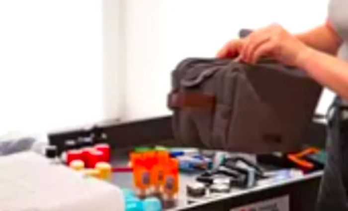 A hand is seen unzipping a Bagsmart Toiletry Bag for Men on a testing cart filled with mini travel-sized items.