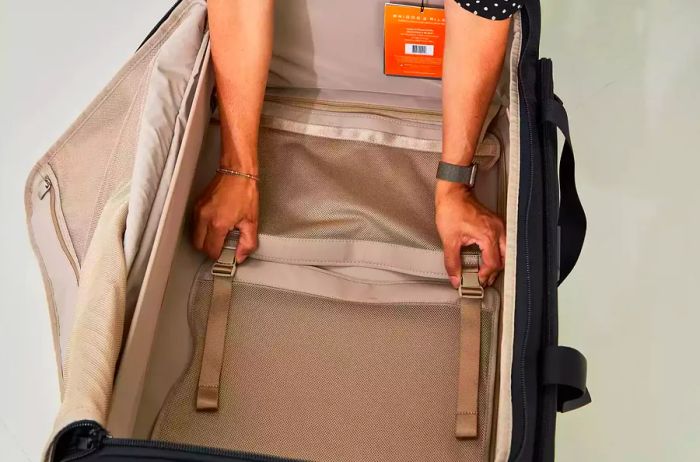 A person adjusts the straps inside a Briggs Riley Baseline Large Two-Wheel 29 inch bag