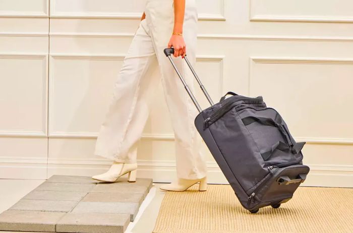 A person rolls the Solo Leroy Rolling Duffel across a rug