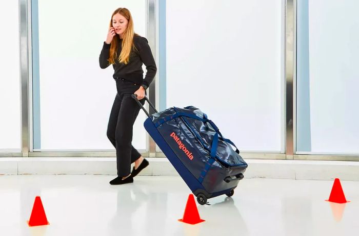 Individual maneuvering the Patagonia Black Hole Wheeled Duffel Bag 100L around cones during testing