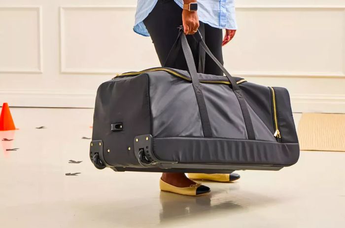 A person raises the Mark & Graham Terminal 1 Checked Rolling Duffle Bag