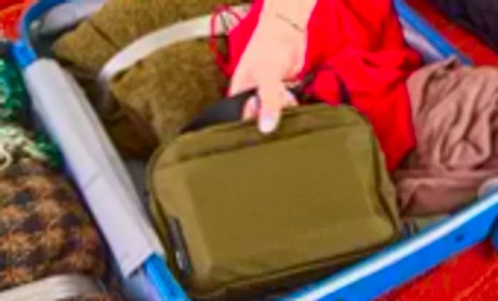 A person stows the Aer Travel Kit 2 into a fully packed suitcase