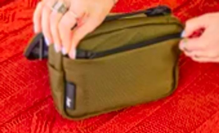 A person secures the front pocket of the Aer Travel Kit 2 by zipping it closed