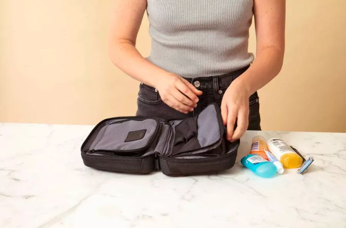 A hand is seen opening the right compartment of the Tumi Response Travel Kit, alongside several travel-sized items.