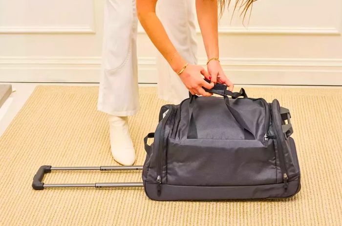 A person adjusts the handle on the Solo Leroy Rolling Duffel for comfort