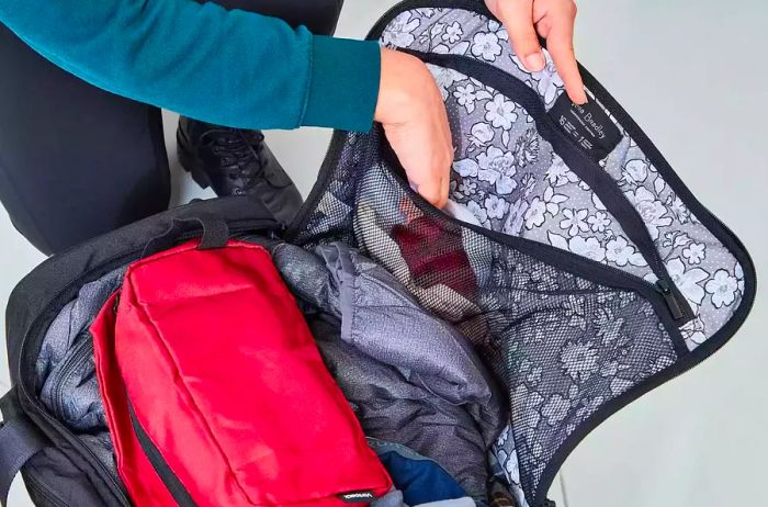 Person stuffing clothing into the zippered section of the Vera Bradley Foldable Rolling Duffel Bag