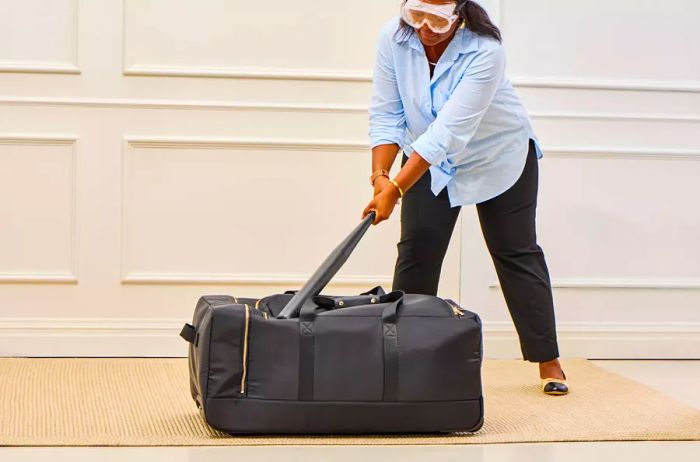 A person strikes the Mark & Graham Terminal 1 Checked Rolling Duffle Bag with a bat