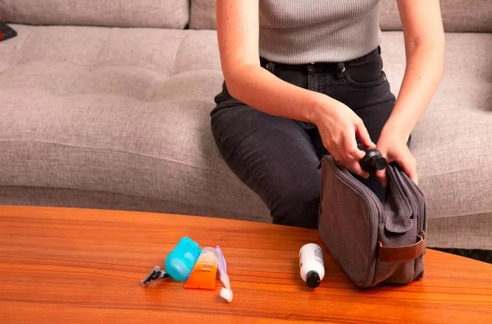 A hand is placing travel-sized conditioner into a Bagsmart Toiletry Bag for Men.