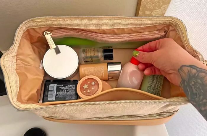 A person inserts a toiletry item into the Beis The Dopp Kit travel pouch