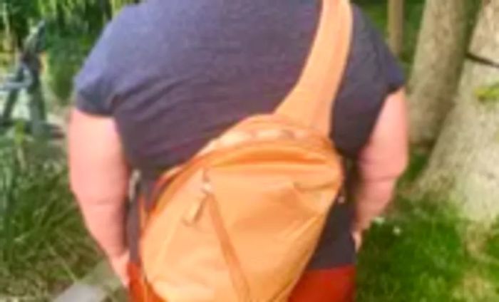 A person carries the orange North Face Women’s Isabella Sling over their back.