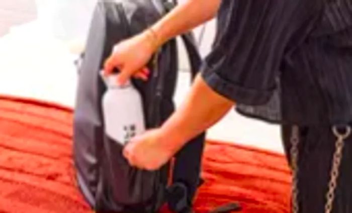 A person puts a water bottle into the side pocket of the Stubble & Co. The Everyday Backpack