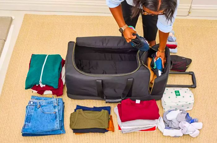 A person is packing the Mark & Graham Terminal 1 Checked Rolling Duffle Bag