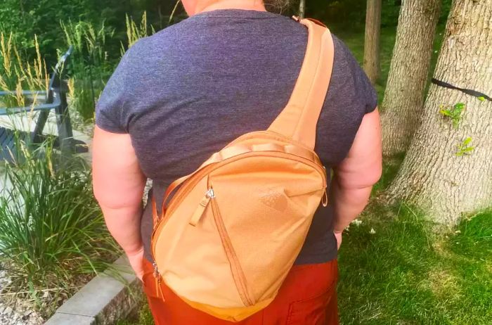 A person carrying the vibrant orange North Face Women’s Isabella Sling on their back.