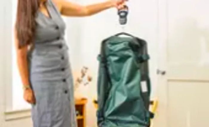 A person checks the weight of the Away The Outdoor Rolling Duffel 85L