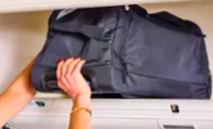 A traveler stores the Solo Leroy Rolling Duffel in an overhead compartment