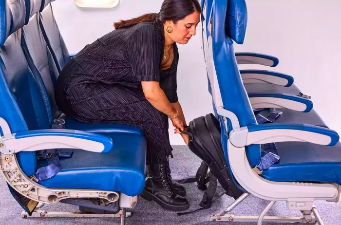 A person places the Stubble & Co. The Everyday Backpack under the seat ahead of them