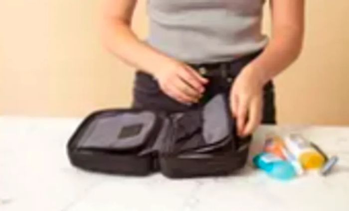 A hand is seen opening the right compartment of the Tumi Response Travel Kit, accompanied by a few travel-sized items nearby.