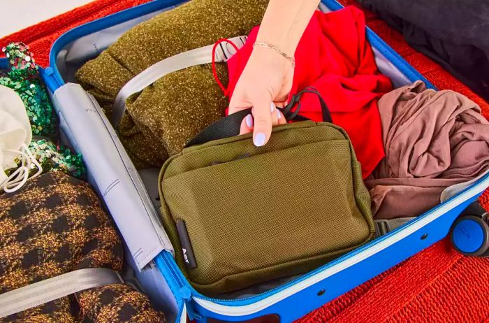 A person adds the Aer Travel Kit 2 to a packed suitcase