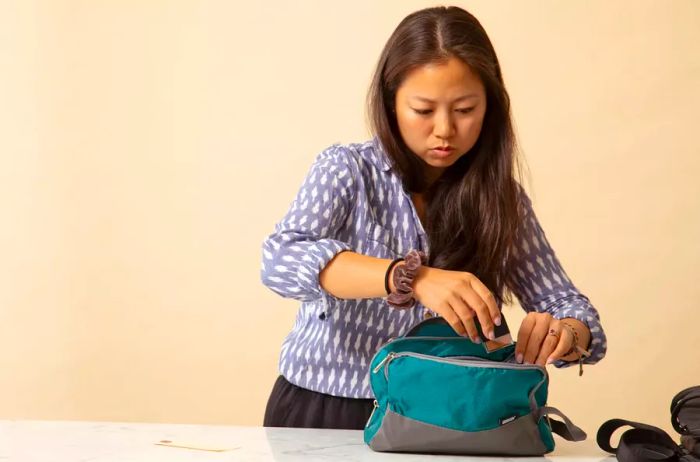 A woman is unzipping a WANDF Toiletry Bag on a countertop