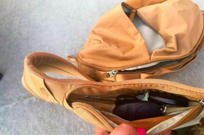 A hand opens the compartment of The North Face Women’s Isabella Sling.