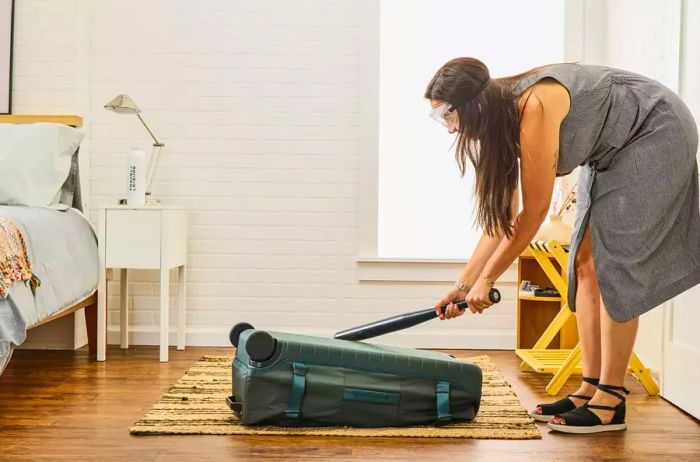 A person strikes the Away The Outdoor Rolling Duffel 85L with a baseball bat