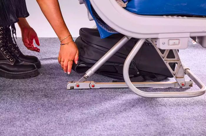 A person positions the Stubble & Co. The Everyday Backpack beneath an airplane seat